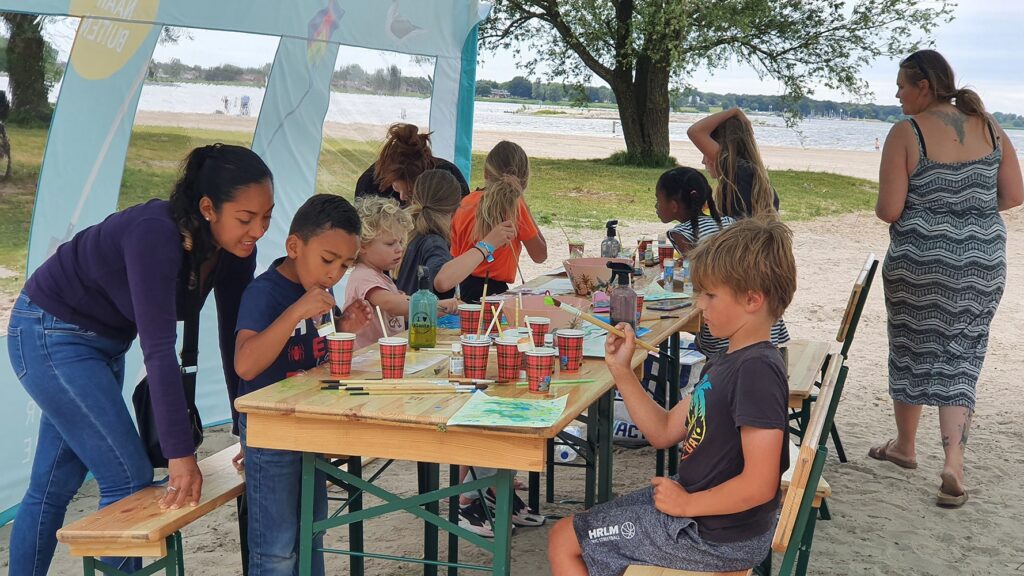 Kinderen zitten aan een tafel op het strand en nemen deel aan een workshop