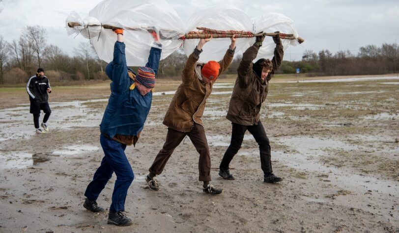 Drie mensen houden stokken met daaraan plastic boven hun hoofd bij het StrandLAB